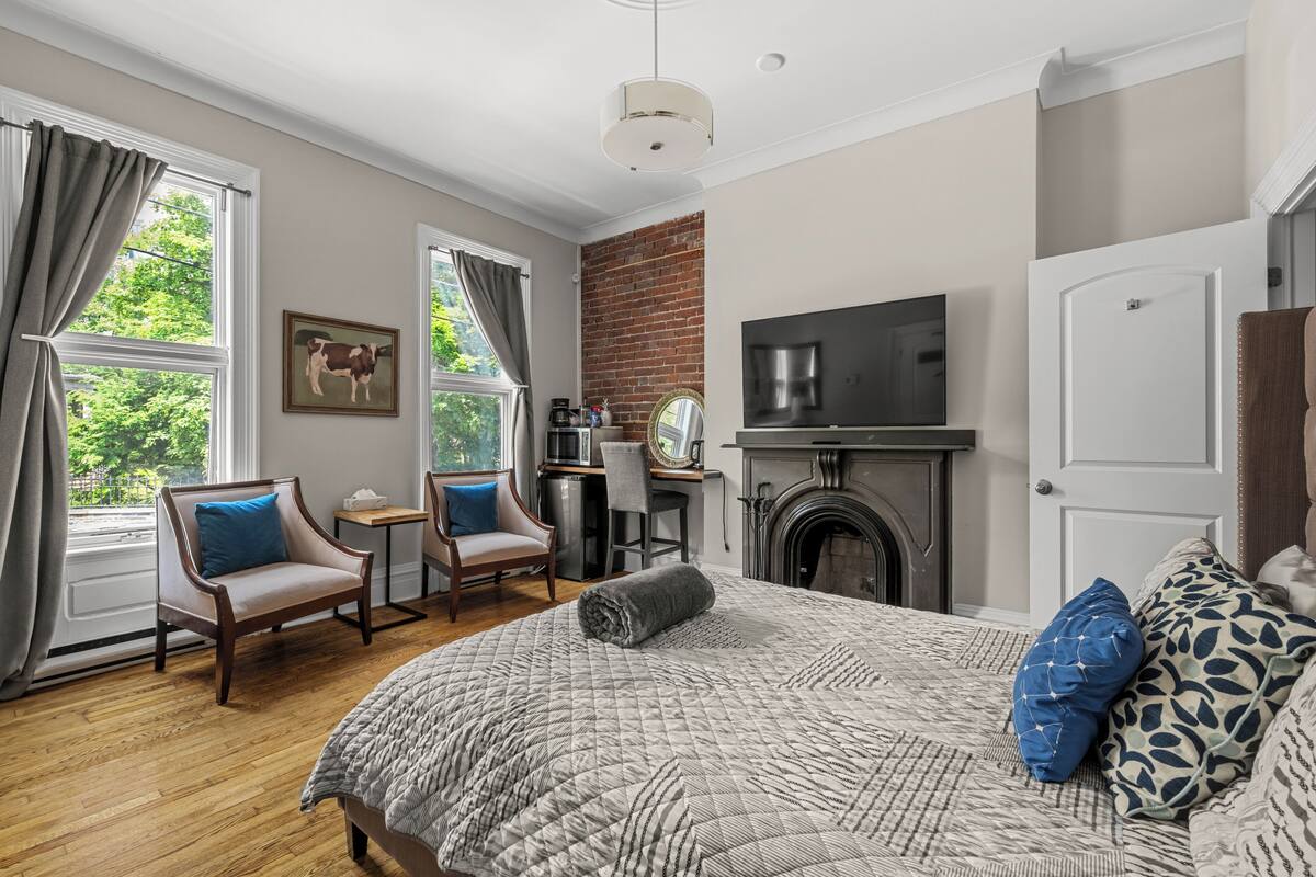 A bedroom with a large bed, a desk, a chair, a TV, and a fireplace.