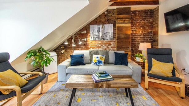 A loft-style living room with a brick wall, a flat-screen TV, a sofa, and a coffee table. - Red George Inn and Suites (Halifax)