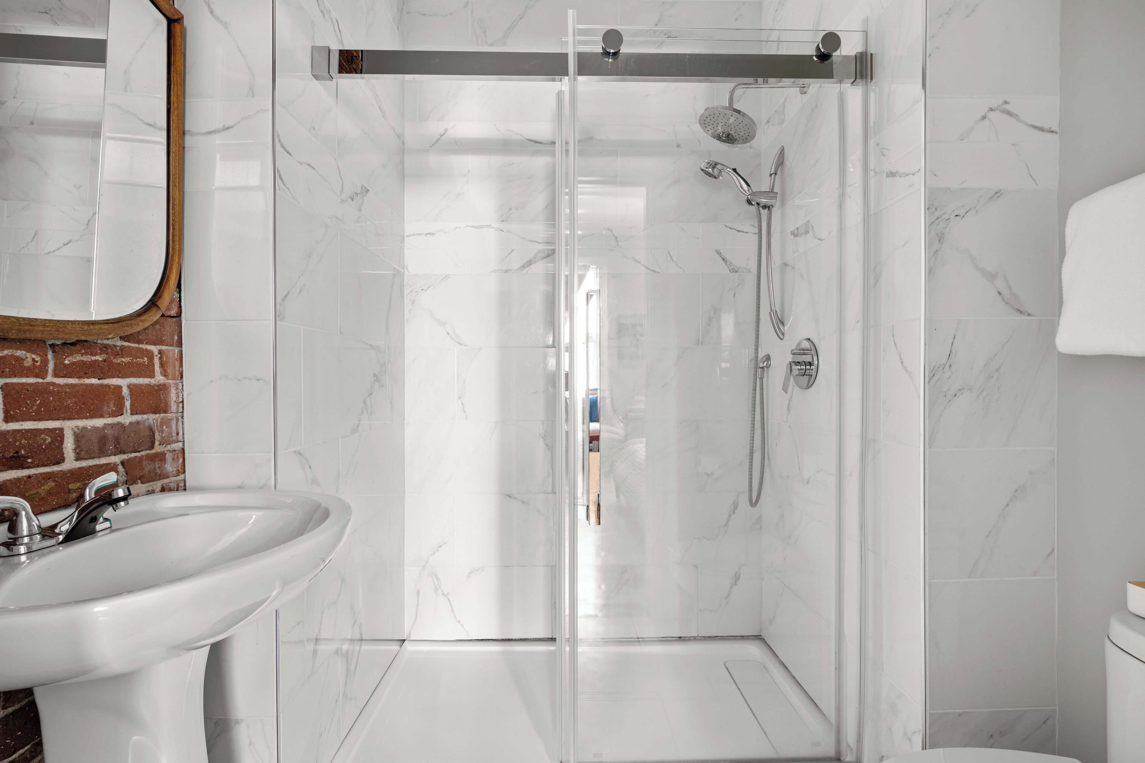 A modern bathroom with a glass-enclosed shower, a white sink, and a marble-tiled wall.