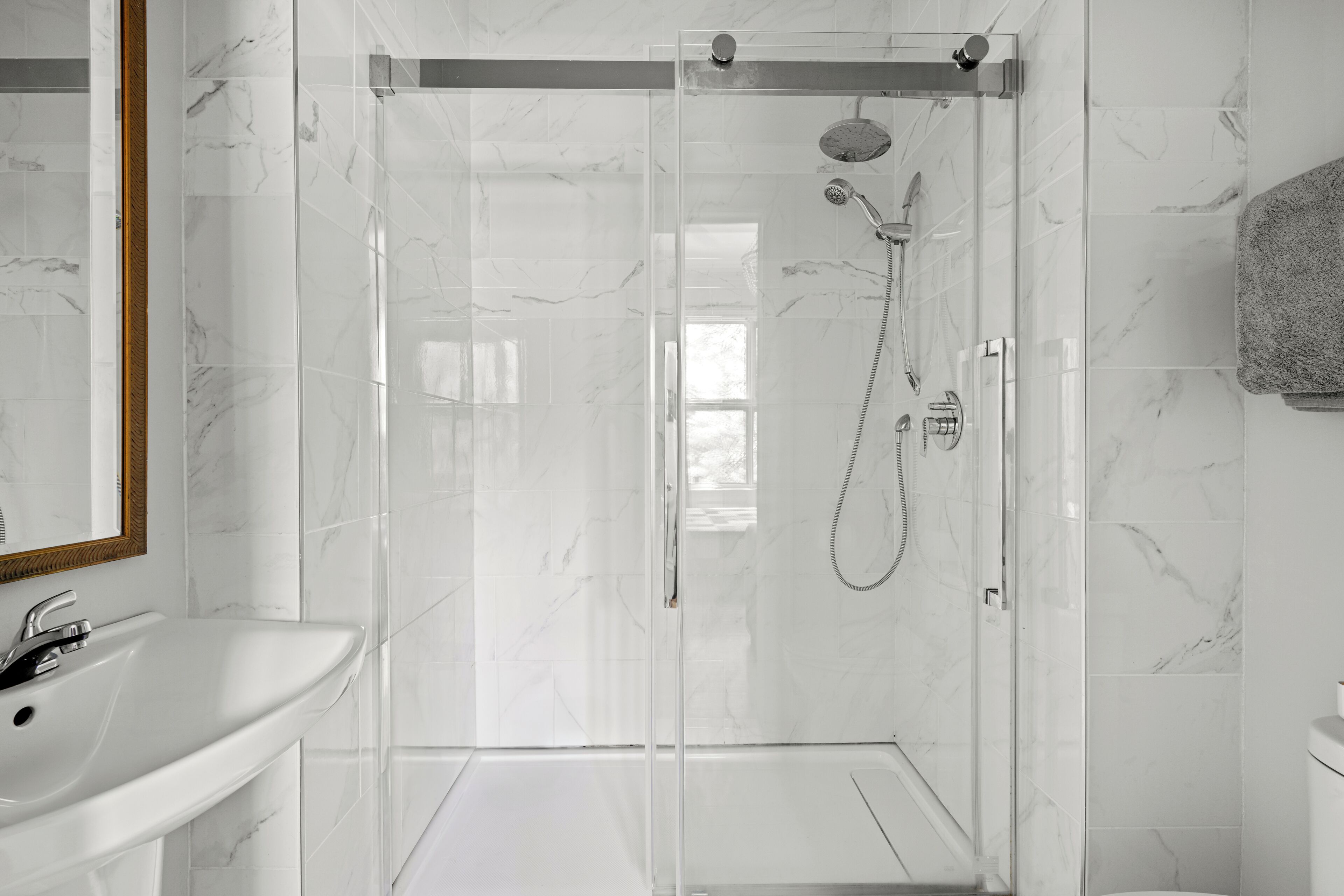 A modern bathroom with a glass-enclosed shower, a white sink, and a marble-tiled wall.