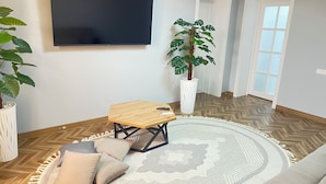 Een woonkamer met een flatscreen televisie, een houten salontafel, een rond vloerkleed en een potplant.