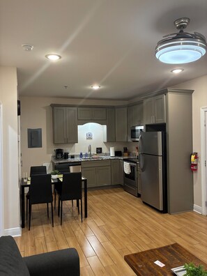 Une cuisine moderne avec des meubles gris, un réfrigérateur en acier inoxydable et un coin repas comprenant une table et des chaises.