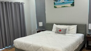 Une chambre bien rangée, avec un lit, un ventilateur de plafond, un tableau et une fenêtre avec des stores.