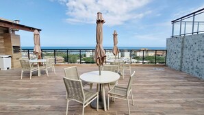 A rooftop terrace with a round table and chairs, two umbrellas, and a view of the sea. - COSTE0109 - Concept Life Stella (Salvador)