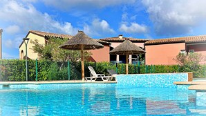 A swimming pool with lounge chairs and thatched umbrellas, surrounded by a fence and greenery. - Apartment 6 people sea view - Théoule sur mer (Côte d'Azur) - SAVANNAH (Théoule-sur-Mer)