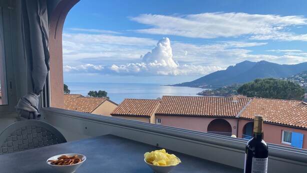 A table with bowls of snacks and a bottle of wine, overlooking a coastal town with terracotta rooftops and mountains. - Apartment 6 people sea view - Théoule sur mer (Côte d'Azur) - SAVANNAH (Théoule-sur-Mer)