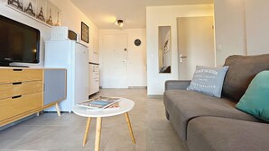 Un espacio habitable compacto con kitchenette, un sofá, una mesa de centro y un televisor.