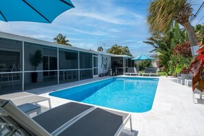 A swimming pool with lounge chairs and umbrellas, surrounded by a building with large windows and a covered patio area. - Villa Maya | Private Neighborhood | Close to Beach (Fort Lauderdale)