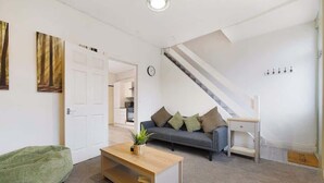 Ein Wohnzimmer mit einer Couch, einem Couchtisch, einer Treppe und einer Tür zu einer Küche.