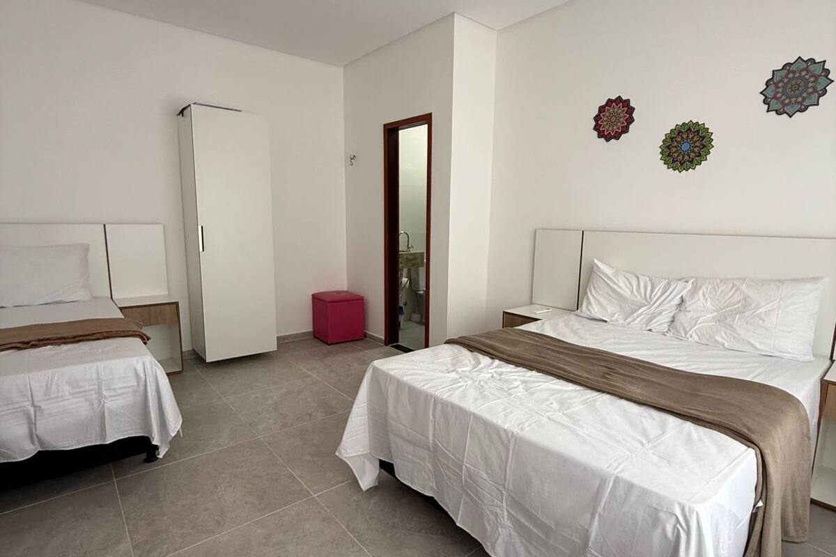 Quarto com duas camas, um guarda-roupa, um espelho e detalhes decorativos nas paredes.