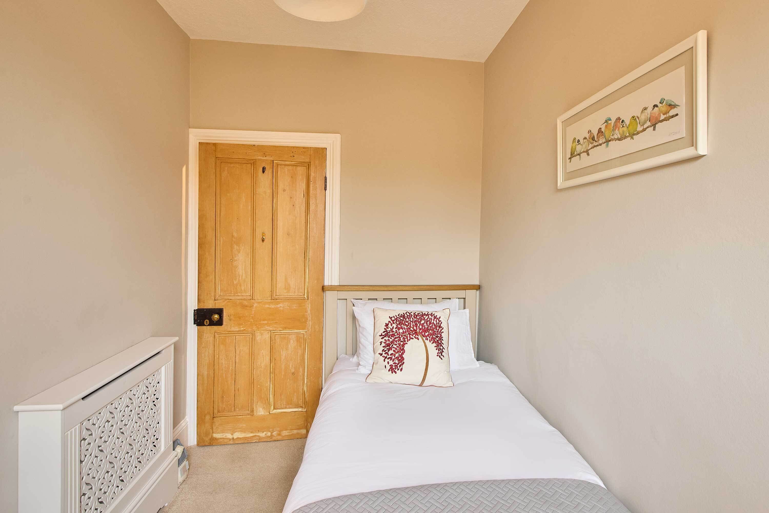 A bedroom with a wooden door, a radiator, a bed with white bedding, and a framed picture on the wall.