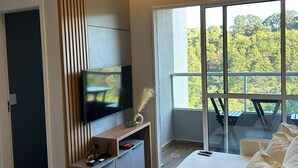 Sala moderna com televisão de tela plana, sofá e varanda com vista para árvores.