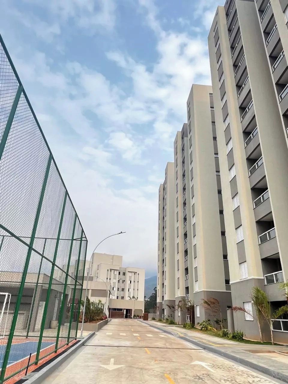 Un edificio residencial de varios pisos con fachada plana, entrada protegida por una reja y camino de entrada pavimentado.