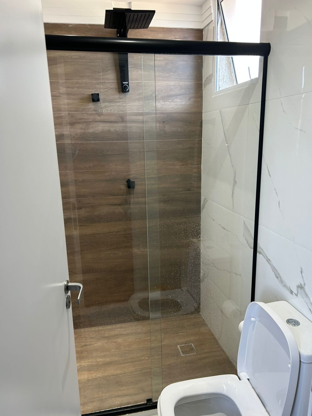 Ein modernes Badezimmer mit einer Glaskabine zur Dusche, einer Toilette und Holzboden.