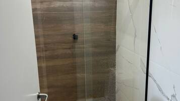 Ein modernes Badezimmer mit einer Glaskabine zur Dusche, einer Toilette und Holzboden.