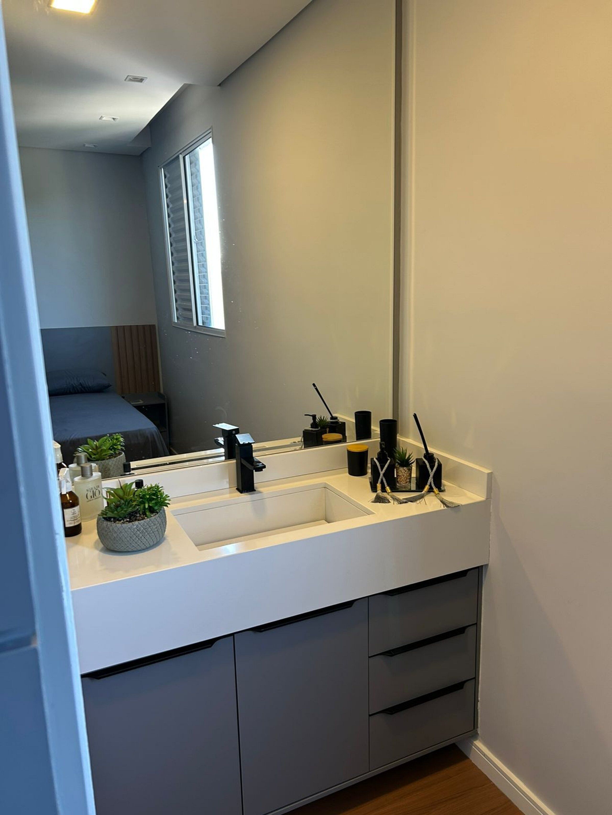 Uma casa de banho moderna com um espelho grande, uma pia branca e um armário embutido.