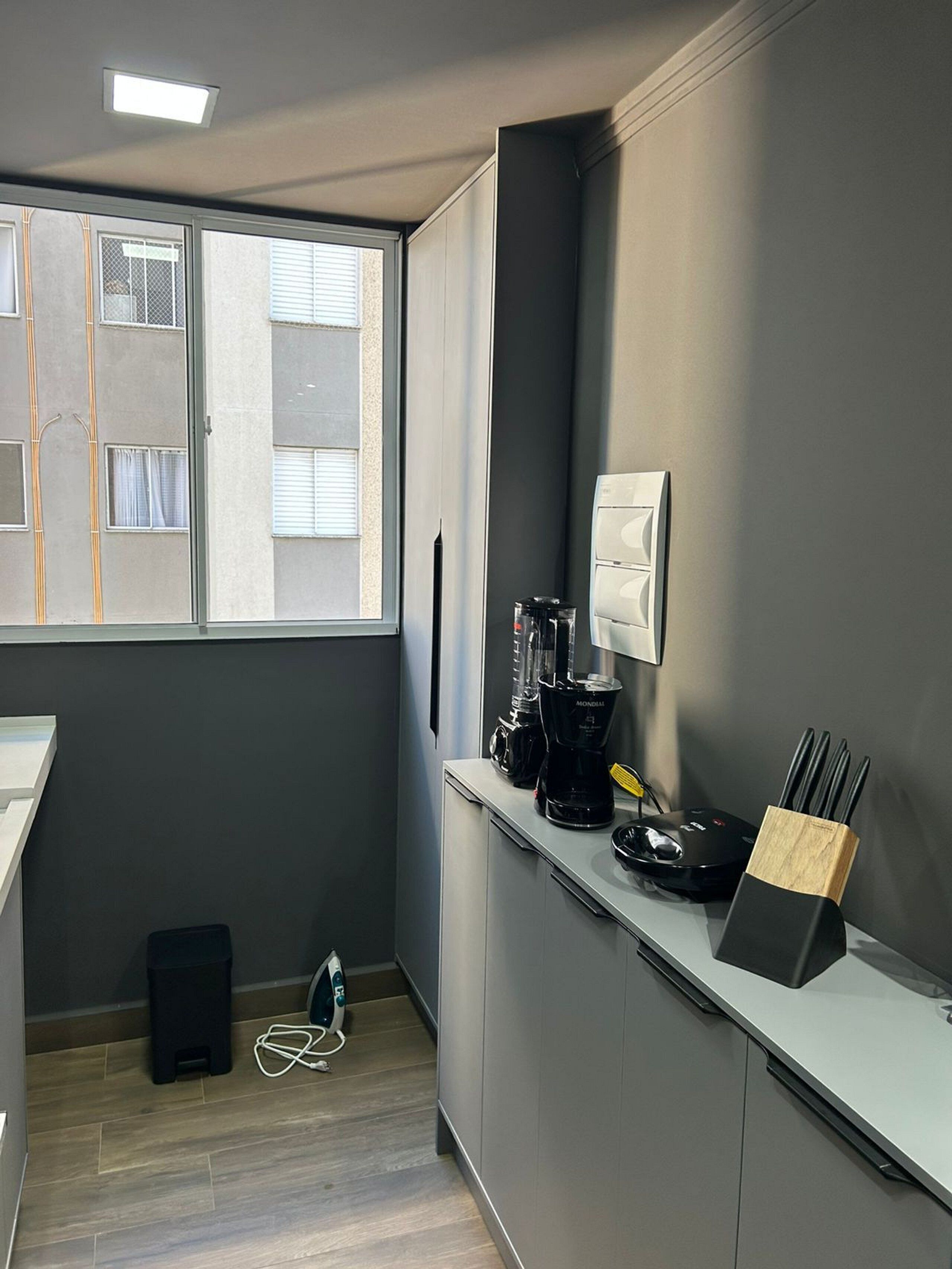 A small kitchenette with a window, a coffee maker, a blender, and a knife holder on the counter.