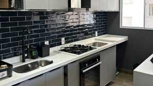 Uma cozinha moderna com armários cinza, painel de azulejos pretos, eletrodomésticos de aço inoxidável e uma janela que proporciona luz natural.