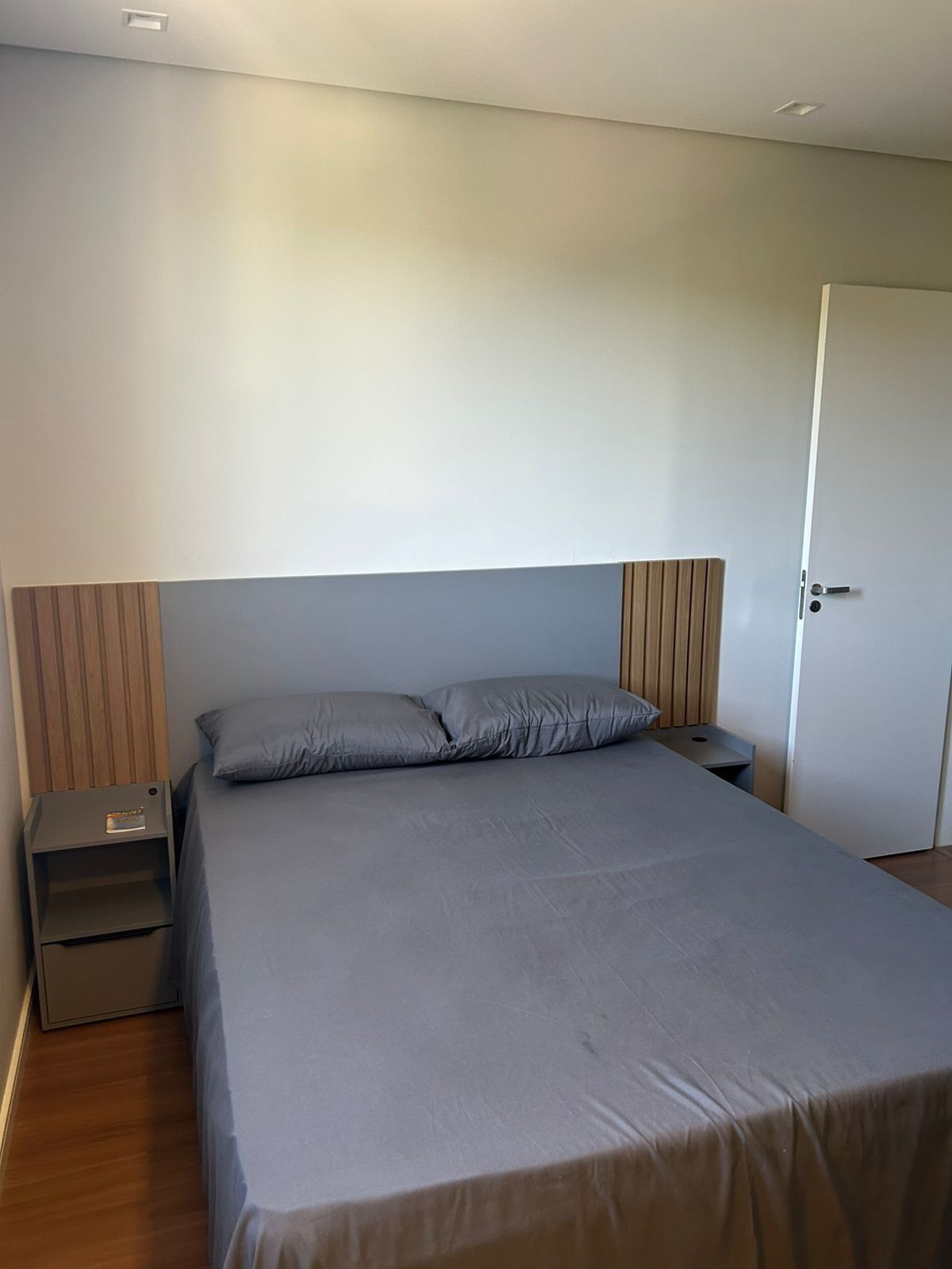 Un dormitorio con una cama individual, una mesita de noche, un cabecero de madera y una puerta.