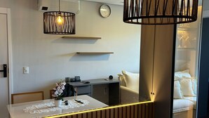 Uma sala de jantar moderna com divisória de madeira, mesa branca com toalha de renda e luminária pendente.