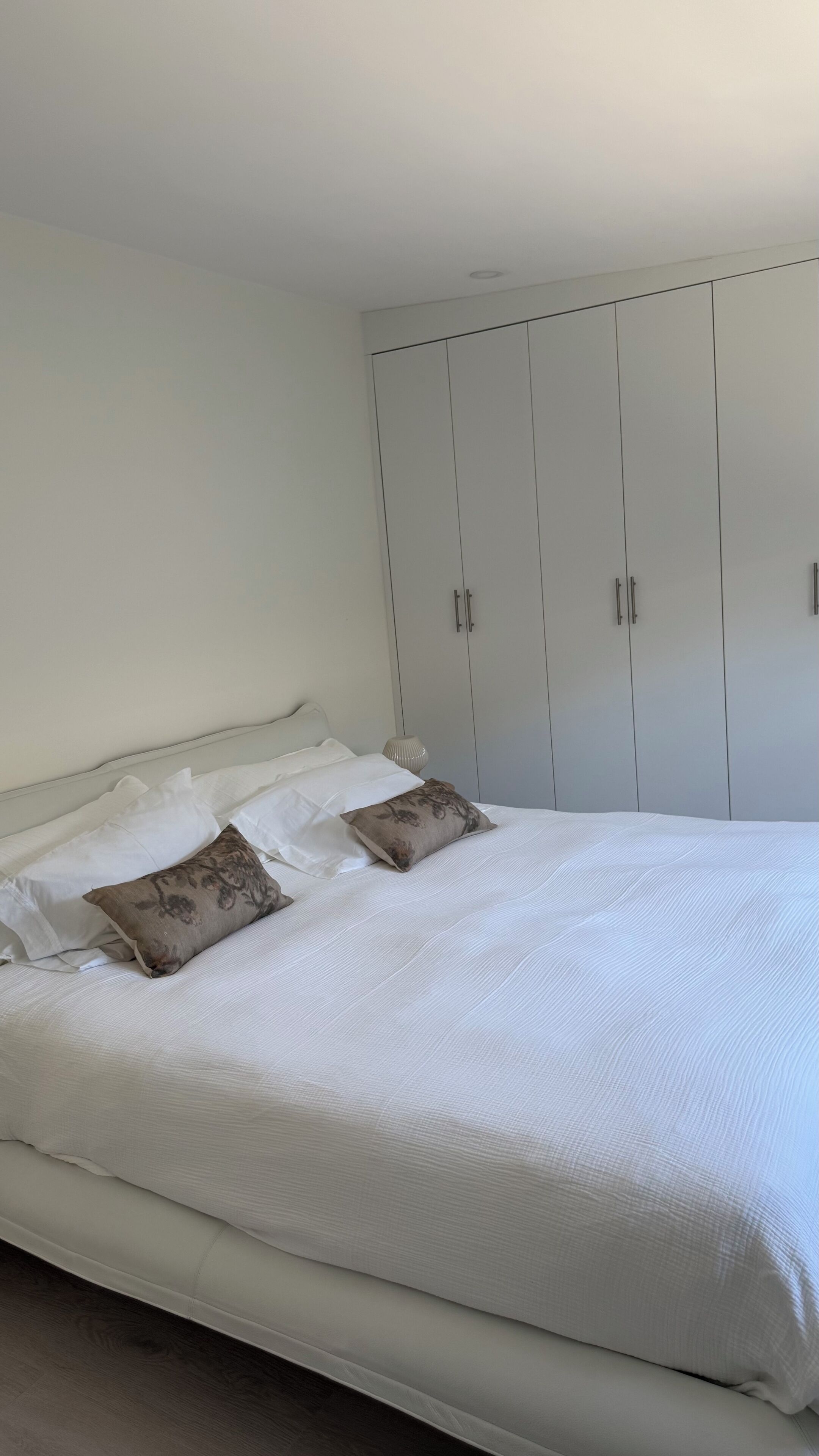 A bedroom with a bed, white bedding, and a wardrobe with two doors.