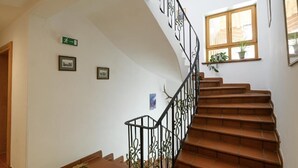 A staircase with a black metal railing, a window with a plant, and a green exit sign on the wall. - Fackler Apartments 1 Riederstein - Relaxed Bavarian Living Near Lake Tegernsee (Tegernsee)