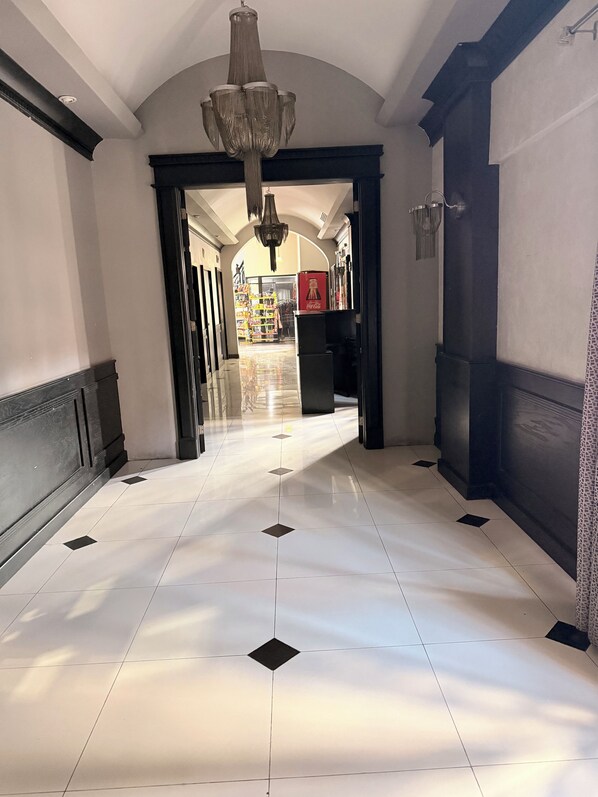 A hallway with a chandelier, tiled floor, and a view into a store area. - Hotel Mirage Express (Matamoros)