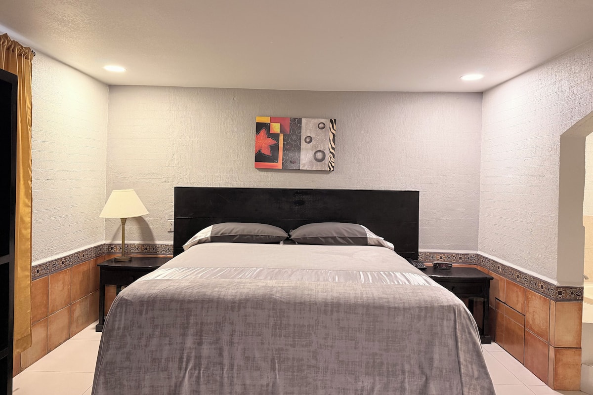 A bedroom with a bed, nightstands, a lamp, and a wall art piece.