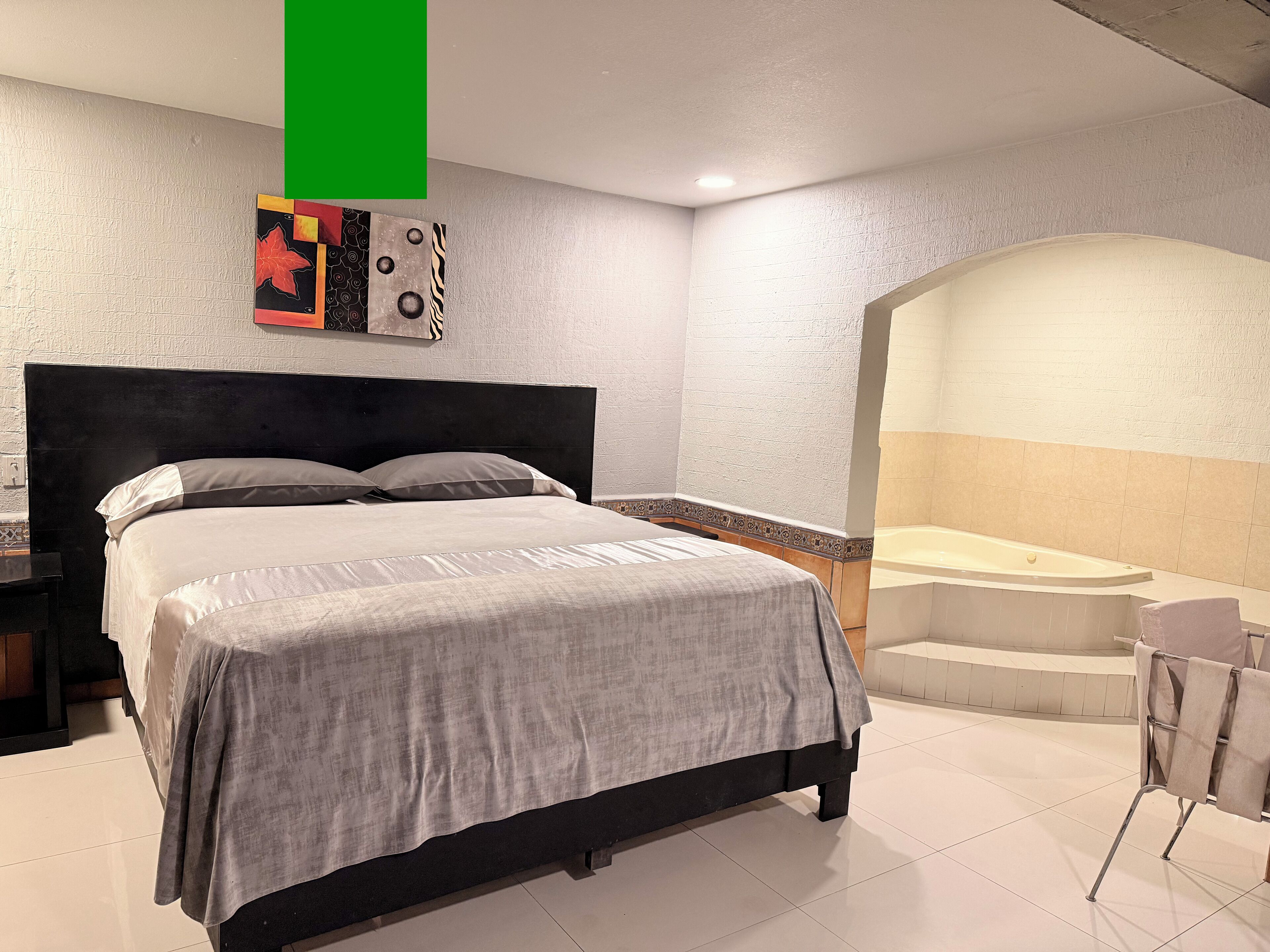A modern bedroom with a large bed, a small table, a chair, and a bathtub.