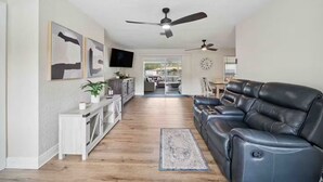 A modern living room with a leather sofa, a TV mounted on the wall, and a ceiling fan. - The Getaway (Spring Hill)