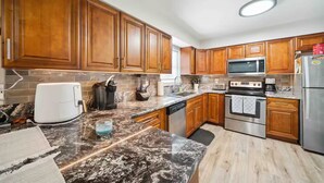 A modern kitchen with wooden cabinets, granite countertops, a built-in microwave, a stainless steel refrigerator, and a dishwasher. - The Getaway (Spring Hill)