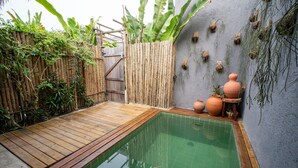 Una pequeña piscina exterior con cubierta de madera, rodeada de bambú y plantas tropicales.