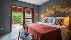 Un dormitorio con cama, una banca, una lámpara de pared y vista a un jardín por una puerta corredera.