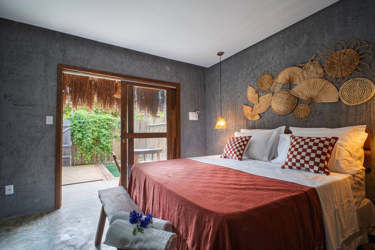 Une chambre à coucher comprenant un lit, un banc, une lampe fixée au mur et donnant sur un jardin grâce à une porte coulissante.