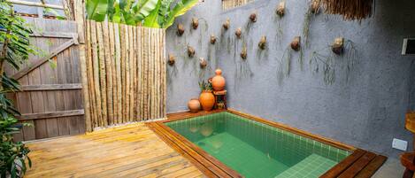 Una terraza de madera con una piscina pequeña, rodeada por una cerca de bambú y un techo de paja.