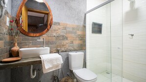 Un baño con salpicadero de baldosas de piedra, un espejo con marco de madera, un lavabo blanco, un inodoro y una cabina de ducha de vidrio.