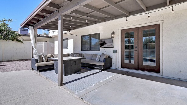 Ein überdachter Patio-Bereich mit einer Couch und einem Tisch, einem großen Fenster und einer Glastür.