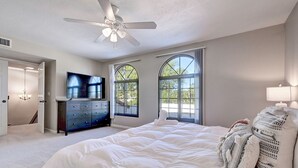 Ein Schlafzimmer mit einem großen Bett, einem Deckenventilator, einem Fernseher und zwei Fenstern.