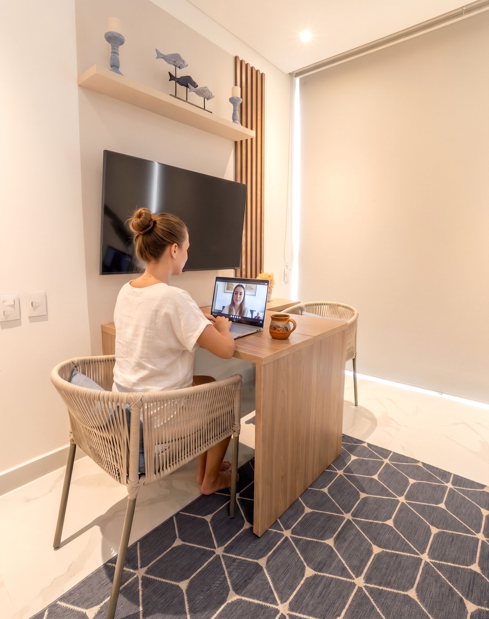 A modern room with a flat-screen TV, a wooden desk, a wicker chair, and a patterned rug.