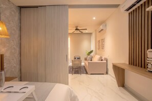 Habitación de hotel con cama, zona de estar con sofá y sillón, una mesita y aire acondicionado instalado en la pared.