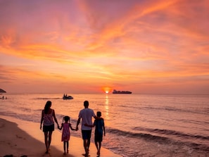A sunset over the ocean with a family walking on the beach.