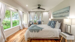 A bedroom with a bed, a ceiling fan, a nightstand, a lamp, and a painting on the wall.
