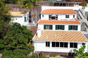 A two-story building with a tiled roof, green shutters, and a balcony. - Mediterranean Style • Sound of Waves • Sunsets (Arco da Calheta)