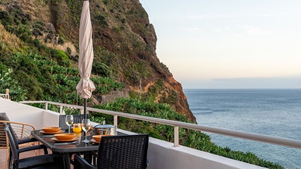 Zona pranzo con tavolo apparecchiato per due, con vista su una scogliera e il mare.