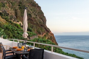 A dining area with a table set for two, overlooking a coastal cliff and the sea. - Mediterranean Style • Sound of Waves • Sunsets (Arco da Calheta)