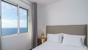 Una camera d'albergo con un letto, un comodino, una lampada e una finestra vista mare.