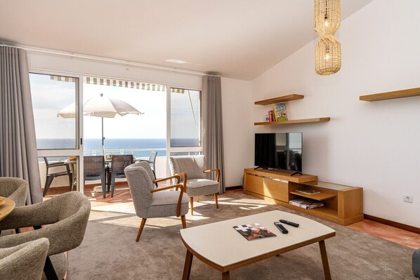 A modern living room with a TV, seating, and a balcony with a view of the sea. - Mediterranean Style • Sound of Waves • Sunsets (Arco da Calheta)