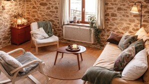 A cozy living room with a stone wall, a rocking chair, a sofa, and a small table with candles.