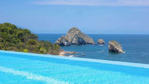 Une piscine d’un bleu éclatant, avec vue sur des formations rocheuses et des bateaux sur l’eau.