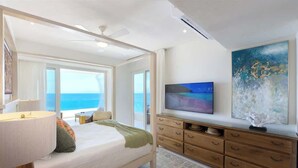 Une chambre à coucher avec un lit, une télévision, une commode en bois et une grande fenêtre donnant sur la mer.